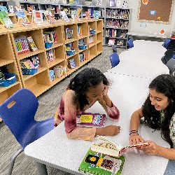 Two HPES students sit a a long library table reading books.